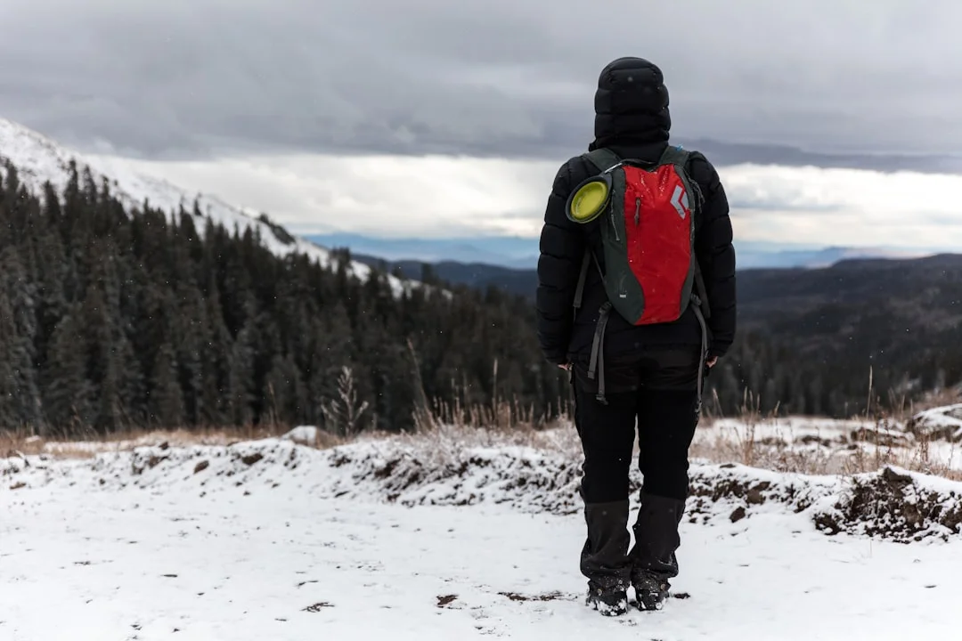 Hypothermia Prevention: What Every Hiker Needs to Know at Highline Trail 2 Winter hiker wearing red hydration pack standing on snowy summit during cloudy conditions