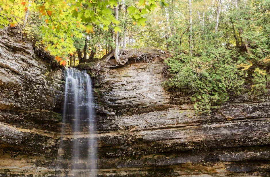 Tahquamenon Falls Winter Hiking Guide (2026) 3 Waterfall cascading down layered rocks with trees in the Upper Peninsula