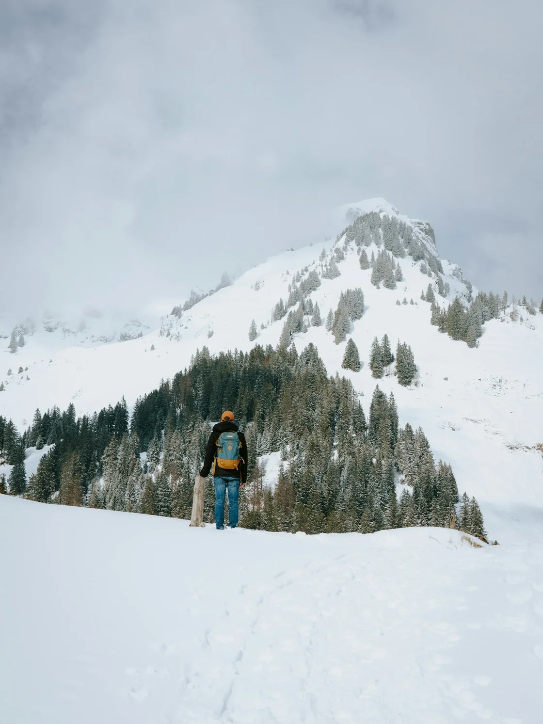 Hiker pausing on a snowy mountainside with winter landscape in background