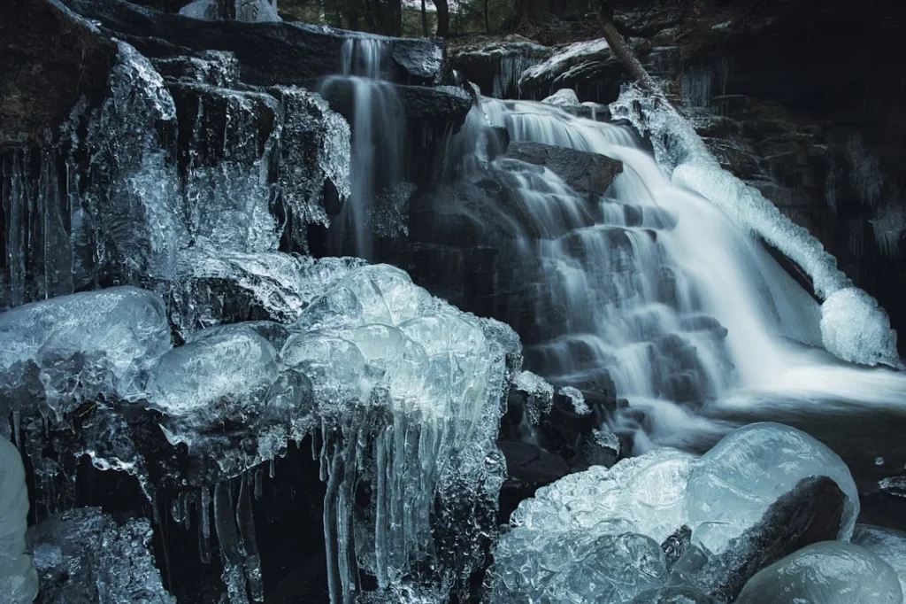 Ricketts Glen winter hiking - massive frozen waterfall with white ice formations cascading down rocky cliff