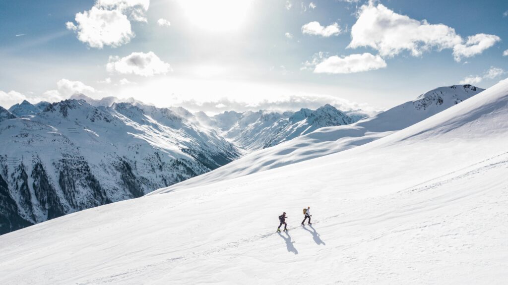 Winter hiking layering system demonstrated by two hikers ascending snow-covered mountain