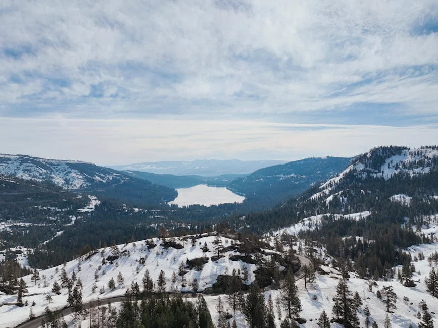 Breathtaking aerial view of Donner Lake surrounded by snow-covered mountains under cloudy sky