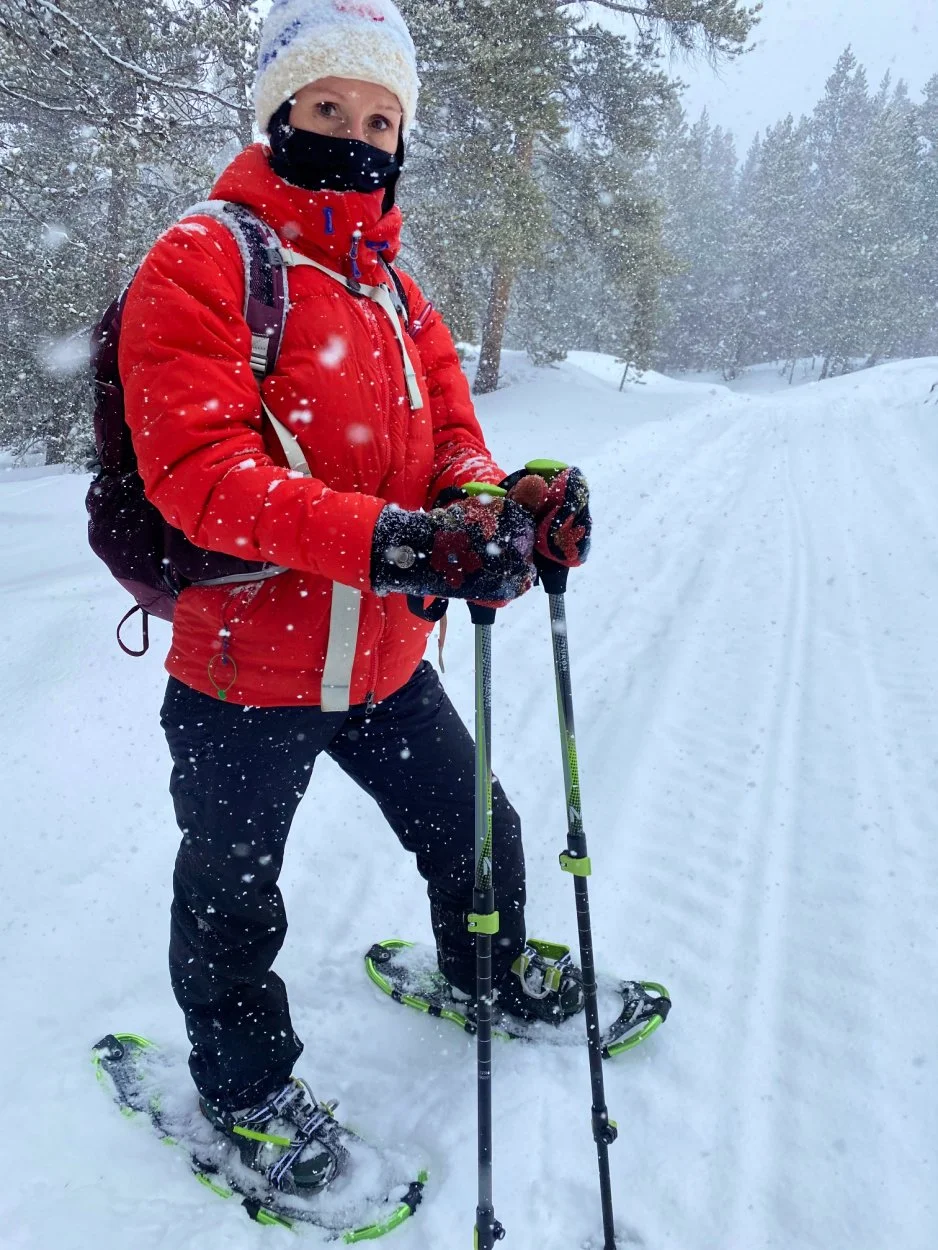 Hiker with trekking poles and snowshoes dressed in red jacket during heavy snowfall on Colorado trail