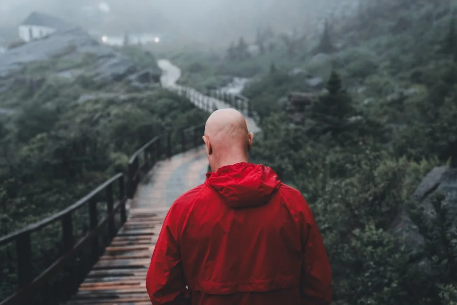 Lone hiker in rain jacket traversing a misty trail during a rainy spring hike